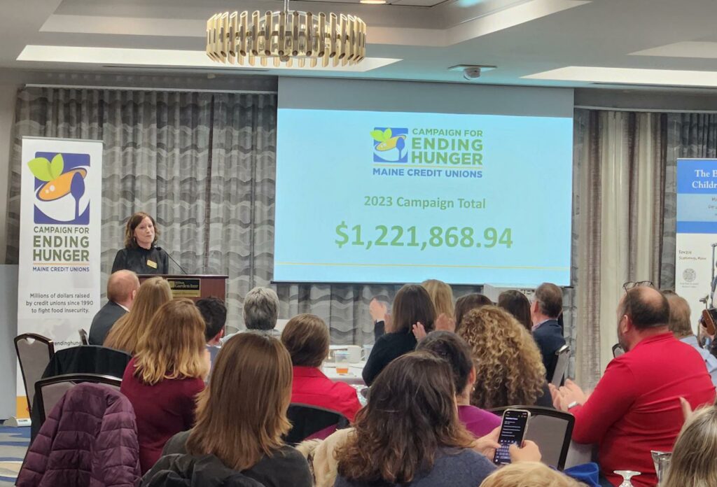 Jennifer Burke, Vice President of Public Relations and Outreach for the Maine Credit Union League, announces the fundraising total of $1,221,868.94 for 2023 in front of a room filled with people.