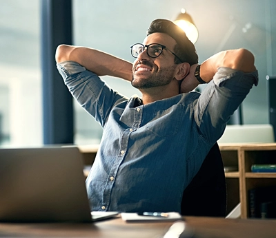 stress free man sitting at his computer with his hands behind his head.